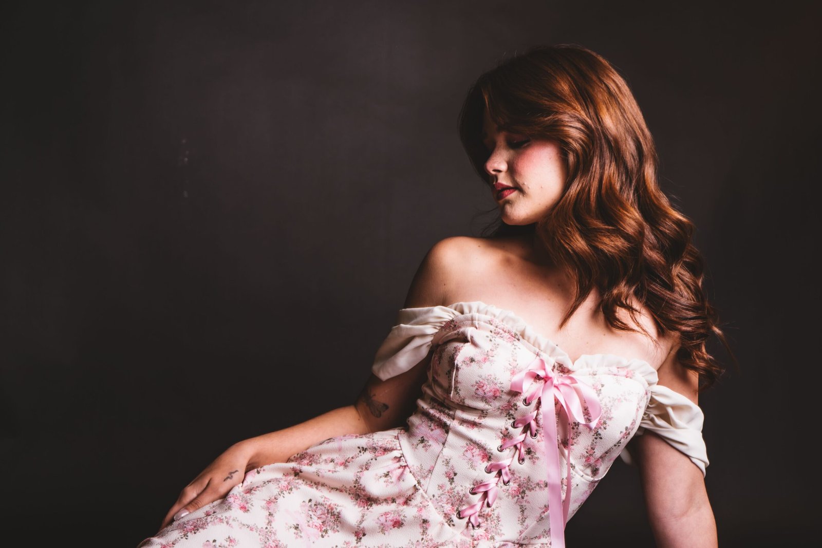 About Us Chic portrait of a woman in a floral corset-style dress against a dark backdrop.
